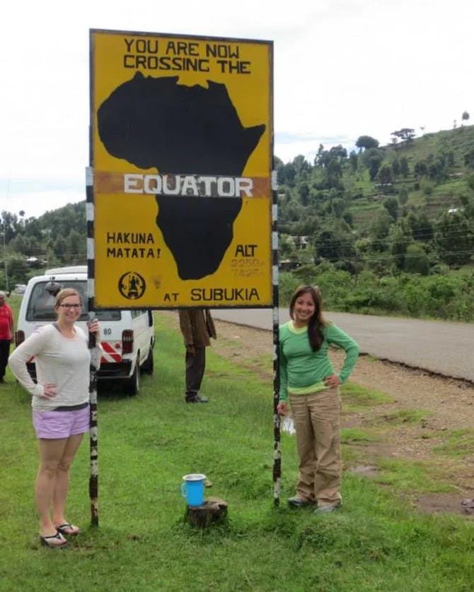 Travel advisor and her friend posing with a yellow board saying "You are crossing the equator"