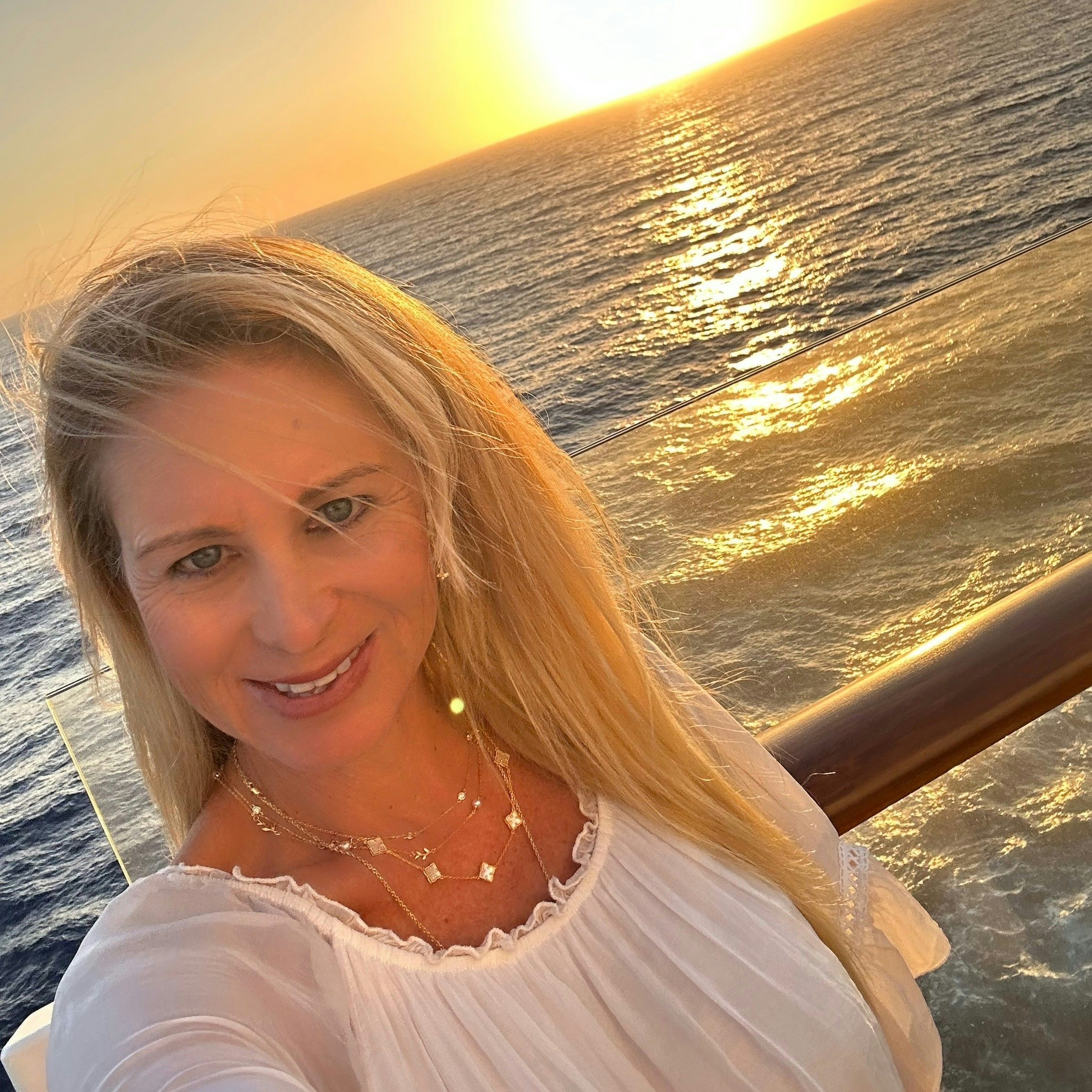 Travel advisor Elaine in white dress posing in front of the ocean at sunset