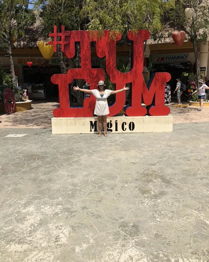 Travel advisor Sharon in a white outfit and hat posing for for a photo with a Tulum sign
