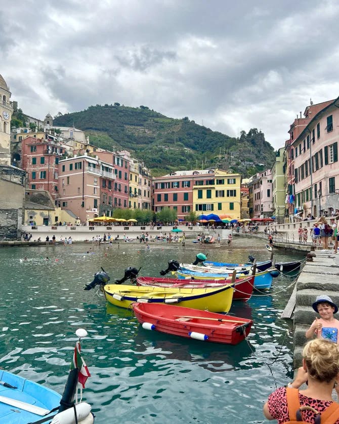 Colorful Italian-style houses on the coast with colorful boats in the water in front.
