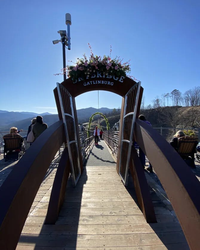 A wooden archway leading to a bridge that overlooks a view of the mountain range. 