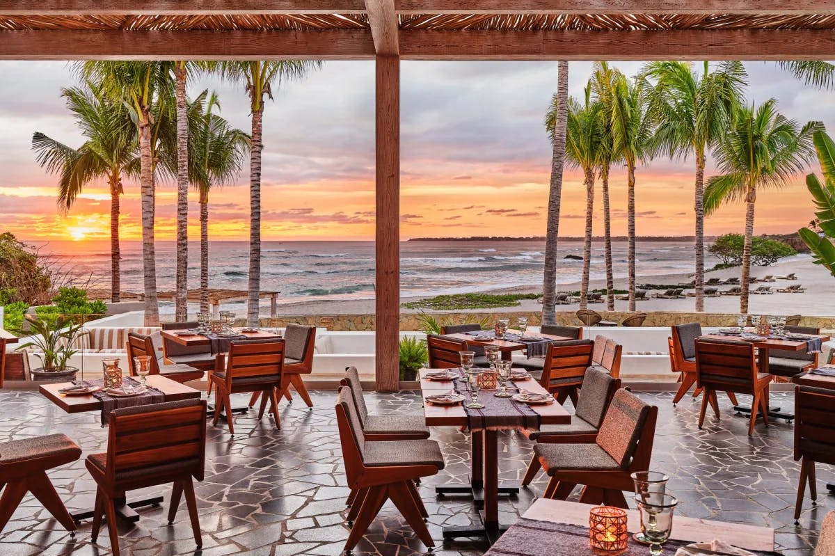 wooden tables dot a dining terrace overlooking the ocean