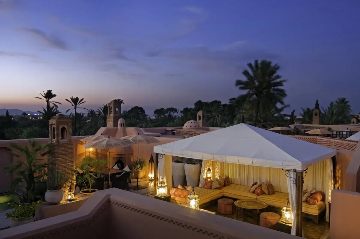At sunset (unseen), palms stand beyond a private courtyard walled off by pink clay. Inside, potted plants and lounge furniture provide an intimate space for guests to relax