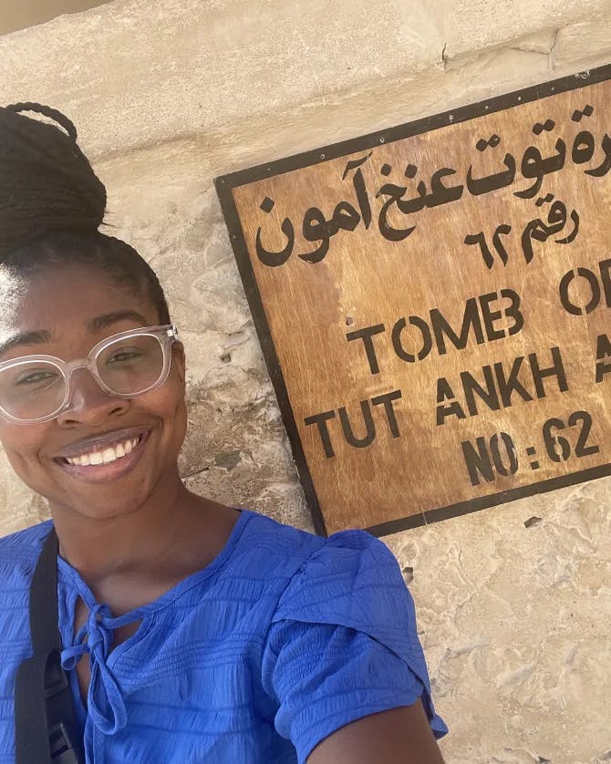Travel advisor Charine in a blue top standing in front of a sign about a tomb in Egypt