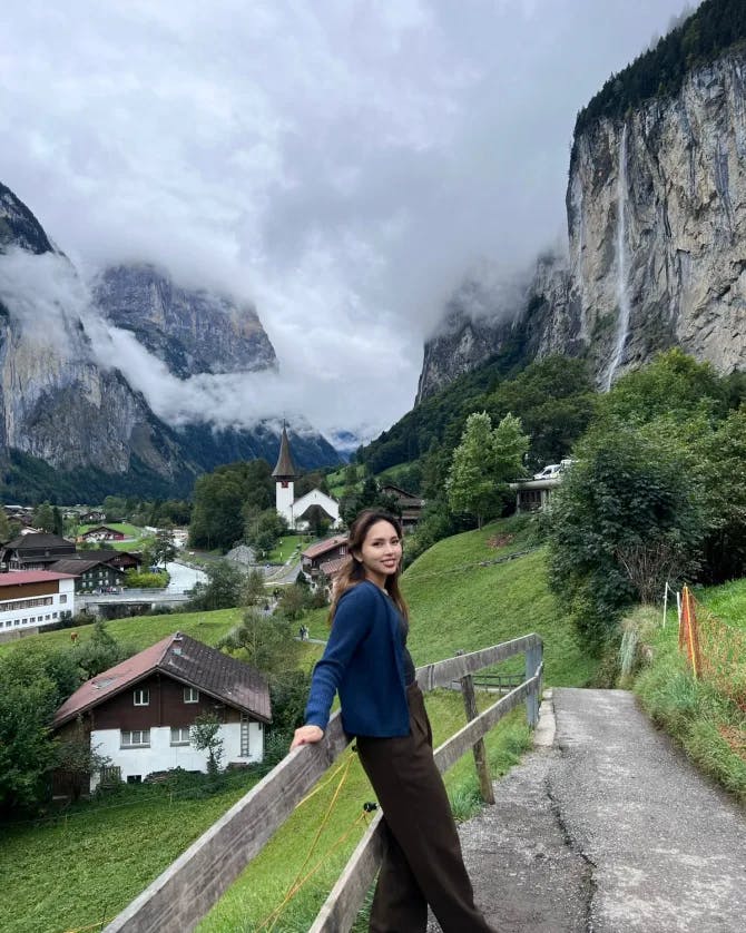 Travel advisor Sharon leaning on a fence with a beautiful view of a town with small buildings and mountains
