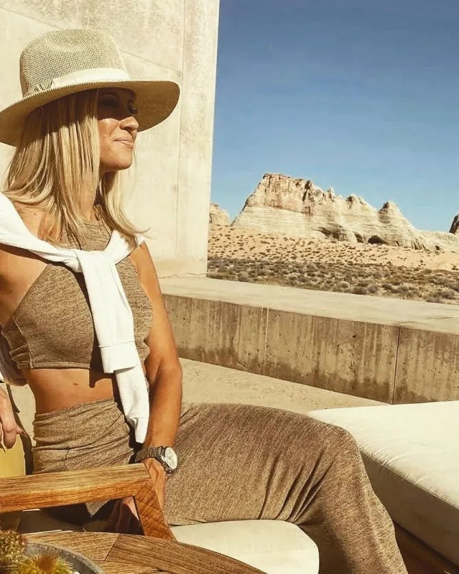 Beatrice wearing a tan skirt and top posing in a chair in front of a desert background.