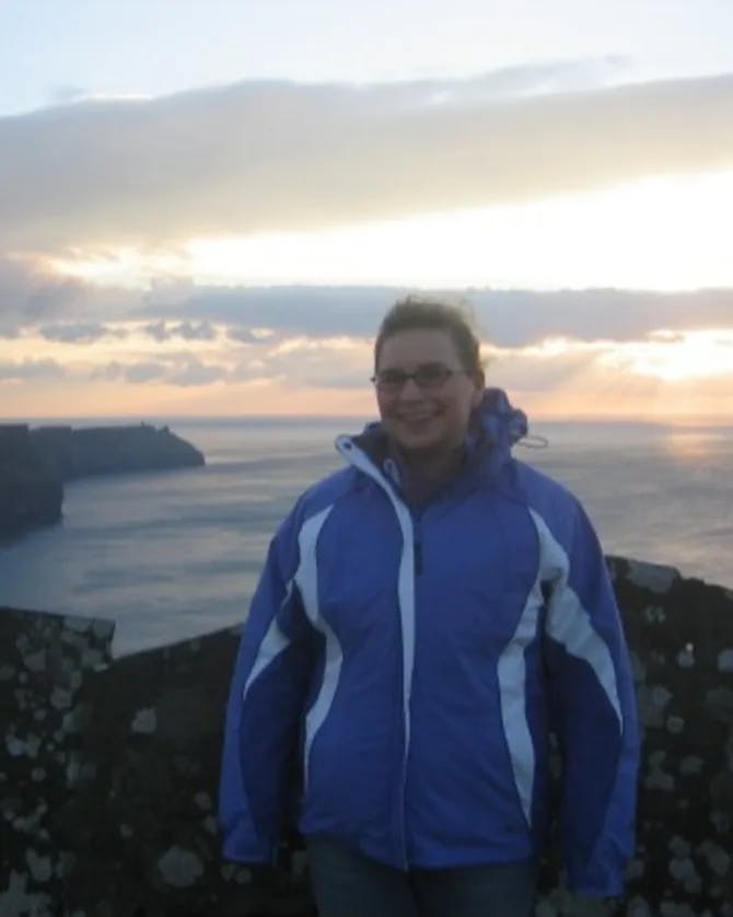 Travel Advisor in blue jacket in front of ocean.