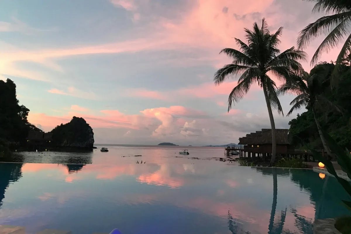 An infinity pool mirrors the pinks and blues of the twilight sky at a luxe beach resort in the Philippines, with palm trees in the distance
