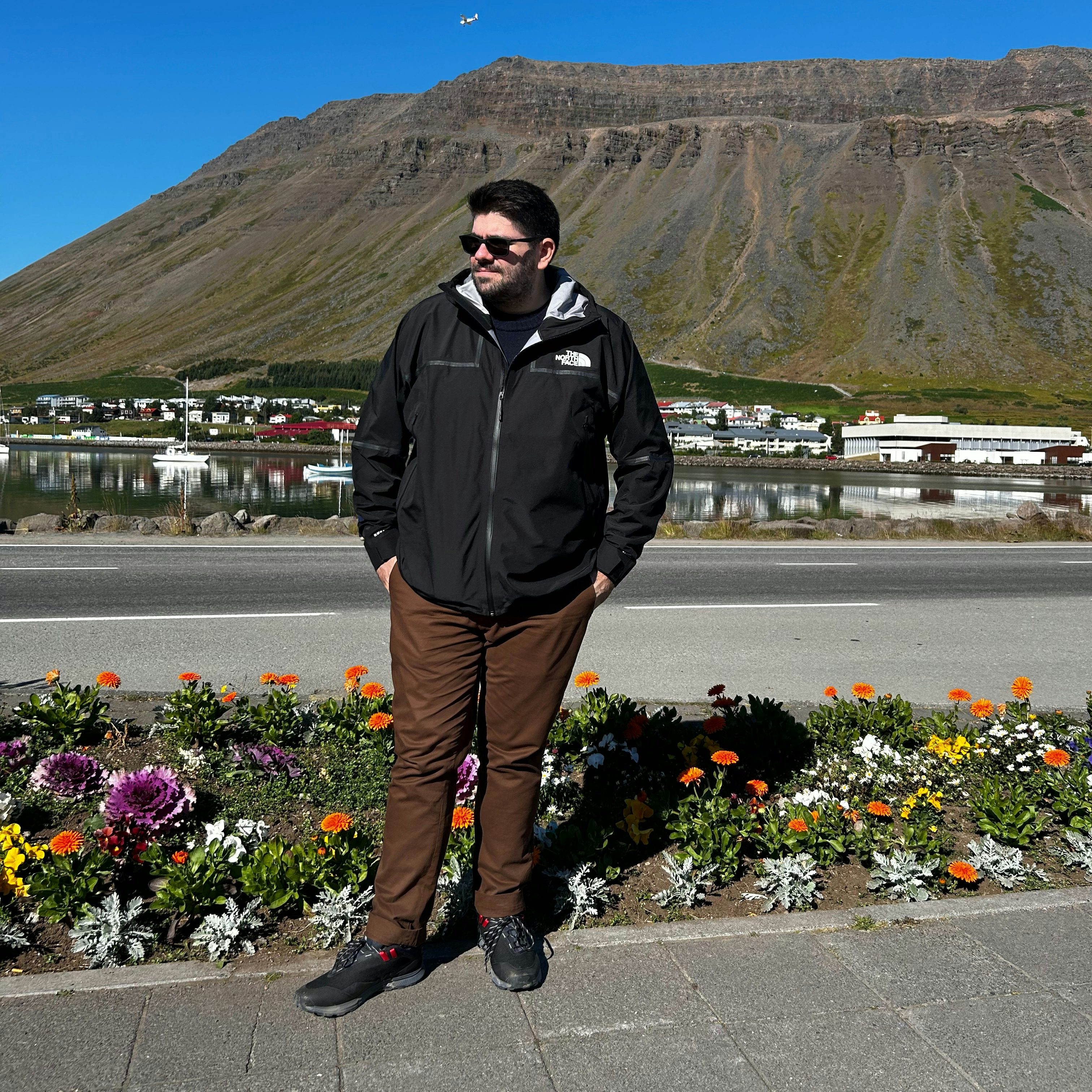 Travel advsior Phil Romanos in a black jacket and sunglasses posing in front of a road with a mountain in view
