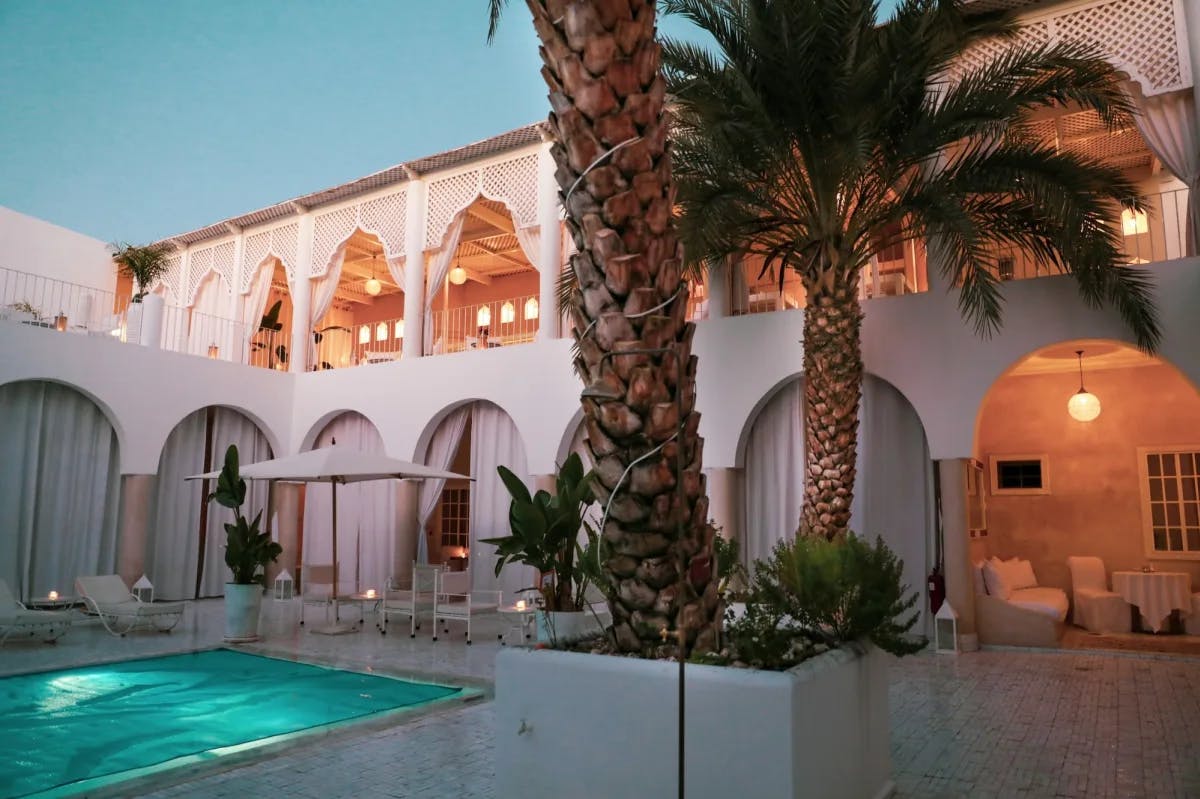 Whitewashed, arched walls surround a lavish courtyard pool and palm garden in a Marrakech riad