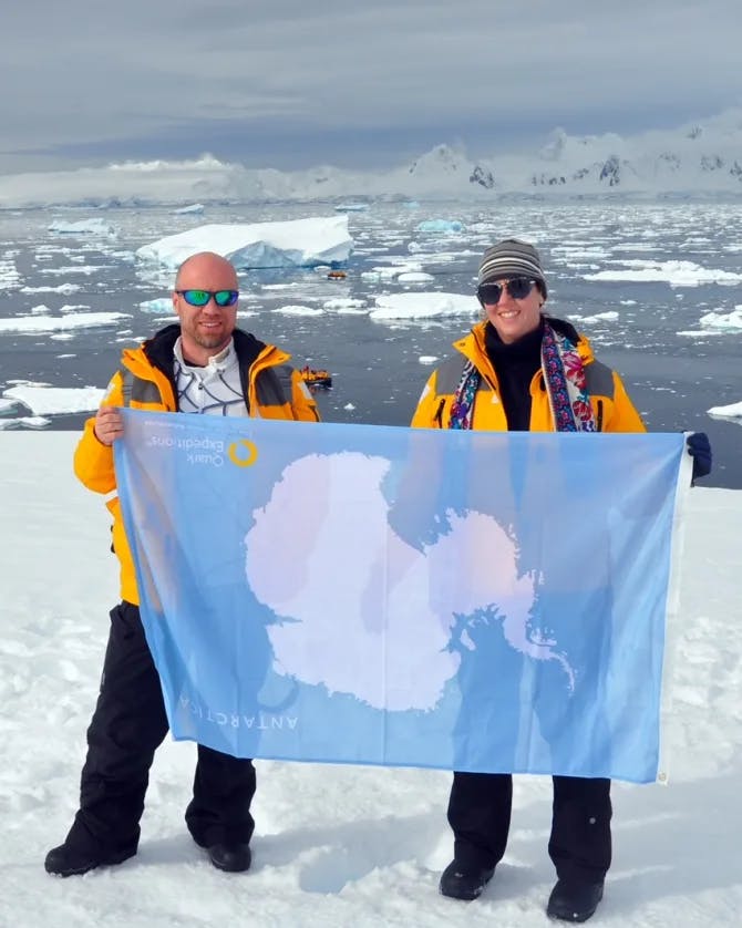 Travel advisor Tammy and male companion in yellow jackets holding a flag in the snow in Antarctica