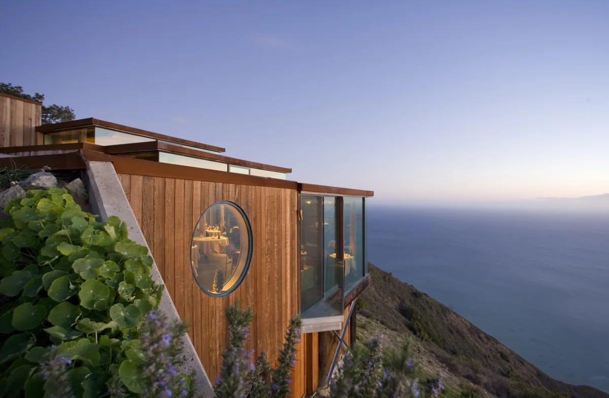a wooden building perched on a cliffside overlooks the ocean