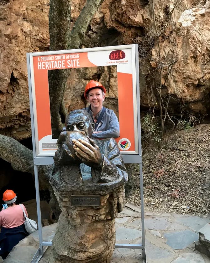 Travel advisor Tammy in an orange helmet posing with photo props and a statue outside with rocky landscape in view
