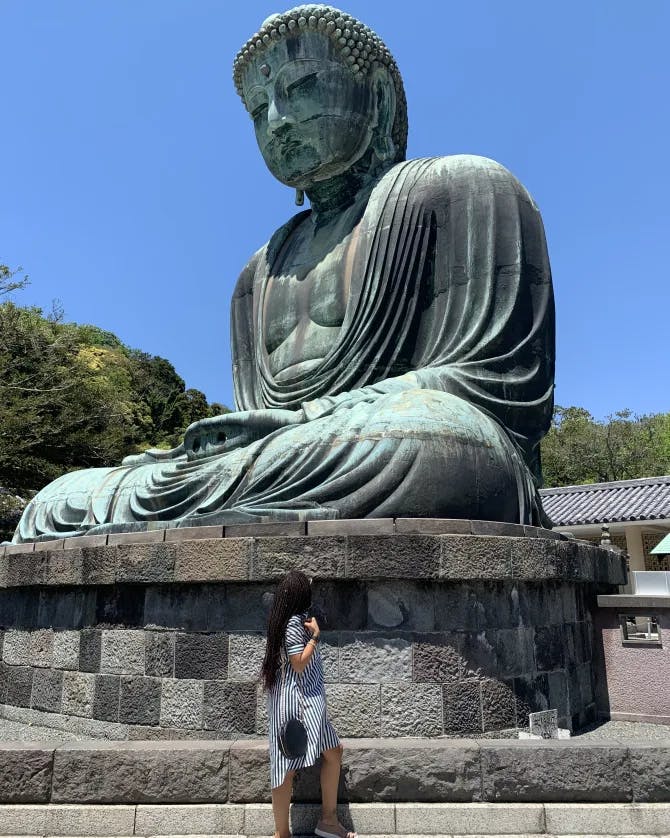 A woman looking up at at a large statue of a Buddha. 