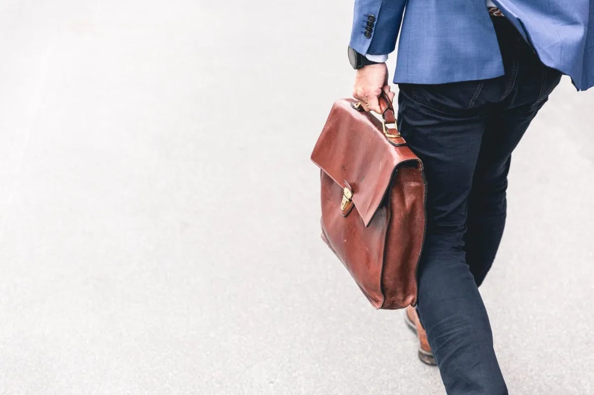 Stylized view of a man walking in high-end business attire, with a focus on his vintage briefcase