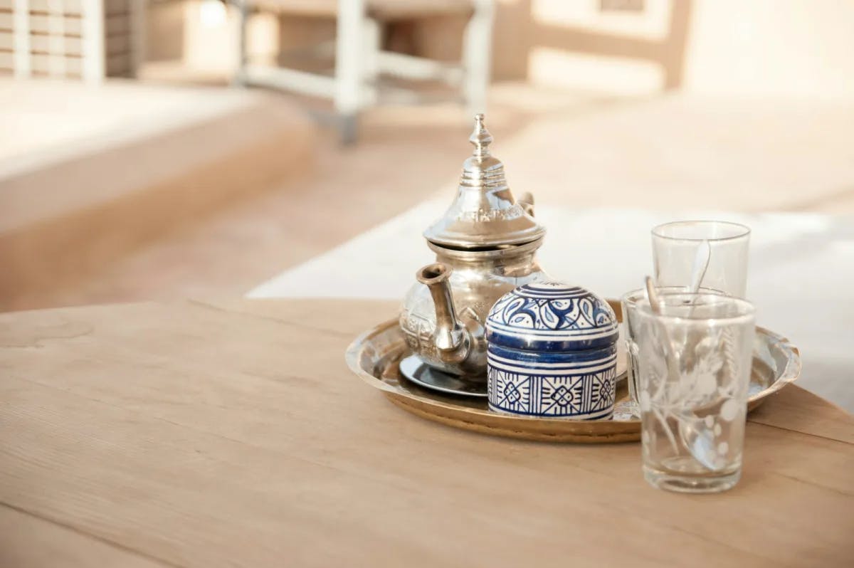 A traditional Moroccan tea set, with metal kettle and ceramic sugar bowl, sitting on a wooden table