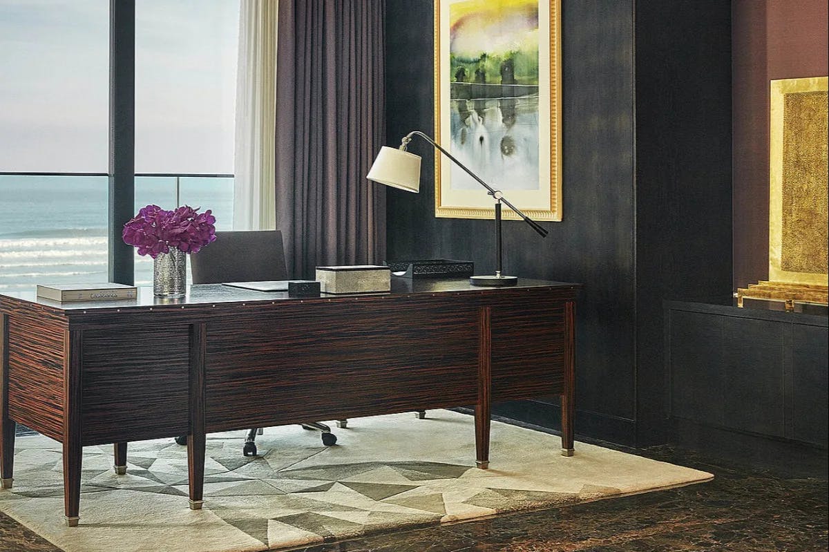 Within a chic room: a hardwood desk sits prominently before bay windows overlooking a Casablanca beach