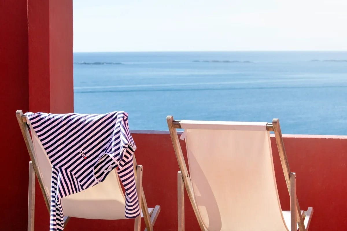 Folding chairs, one with a shirt hanging from it, are set up at a Medeterranean resort to look out over the water