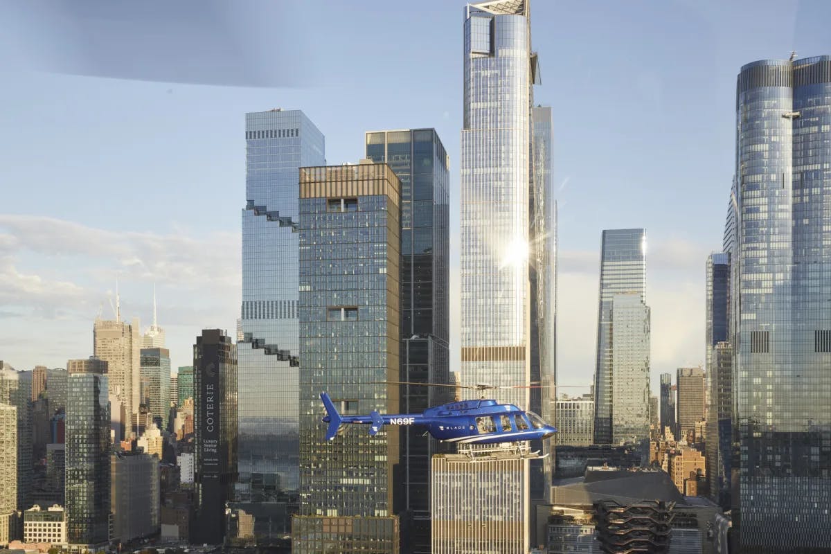 a blue helicopter flies in front of tall shiny buildings on a sunny day