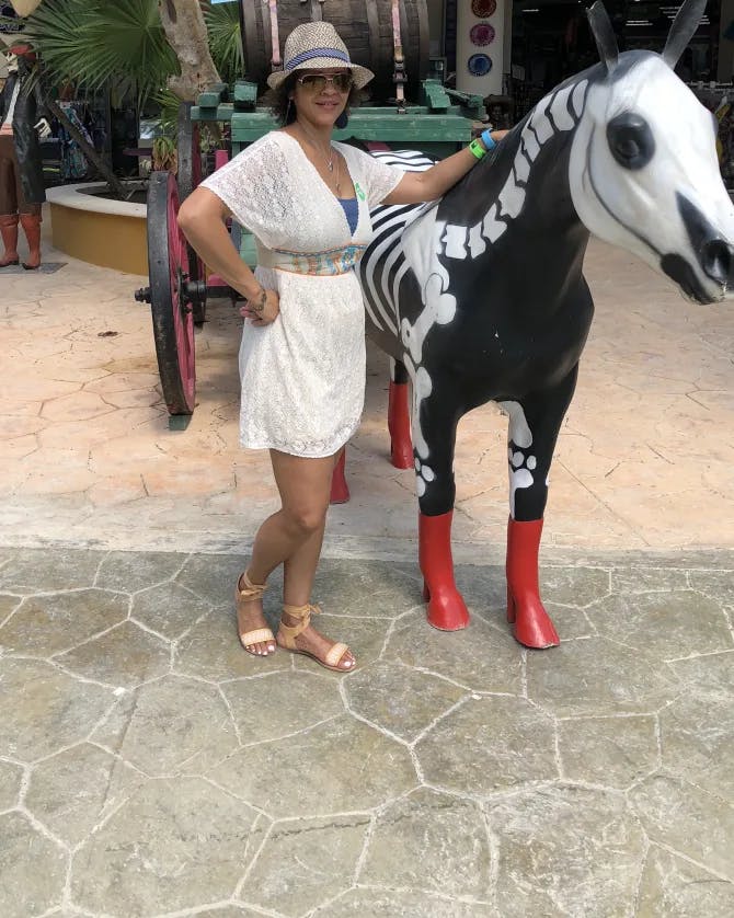 Travel advisor Sharon posing for a photo in a white outfit and hat with a black and white horse statue