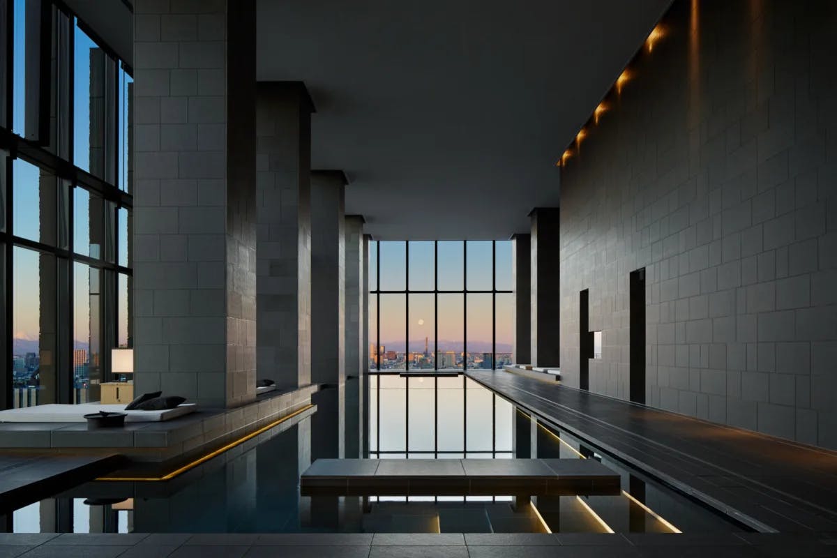 an indoor swimming pool in a sleek room with tall ceilings and large windows overlooking a city