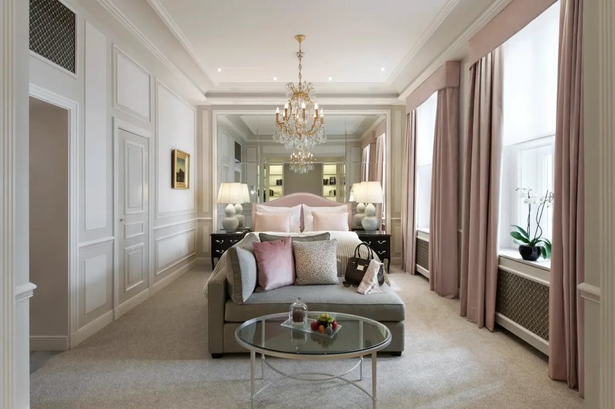 an opulent hotel bedroom with pink drapes and a gray couch with pink velvet pillows