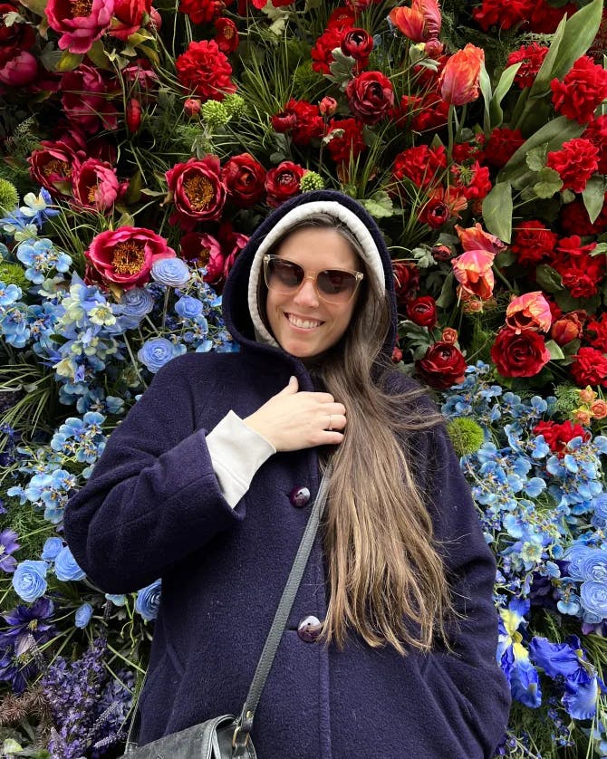 Travel advisor Brittanie posing a photo in a hooded coat in front of beautiful red and blue roses