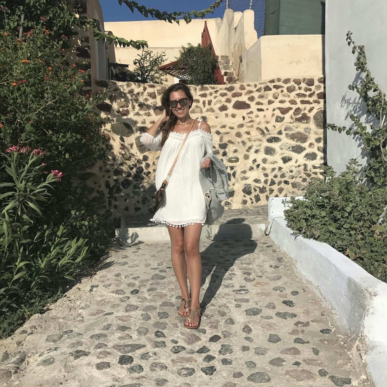 Travel advisor Megan in white dress standing on a cobbled walkway with white wall and buildings in view