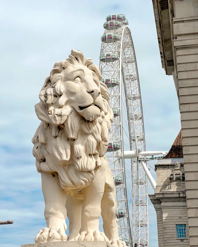 View of a lion sculpture with large ferris wheel behind