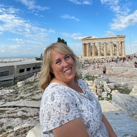 Lisa Coombs in a white top posing in front of ancient archeological site 