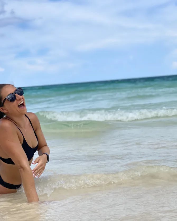 Travel advisor Sarah in black bikini sitting at the ocean shore