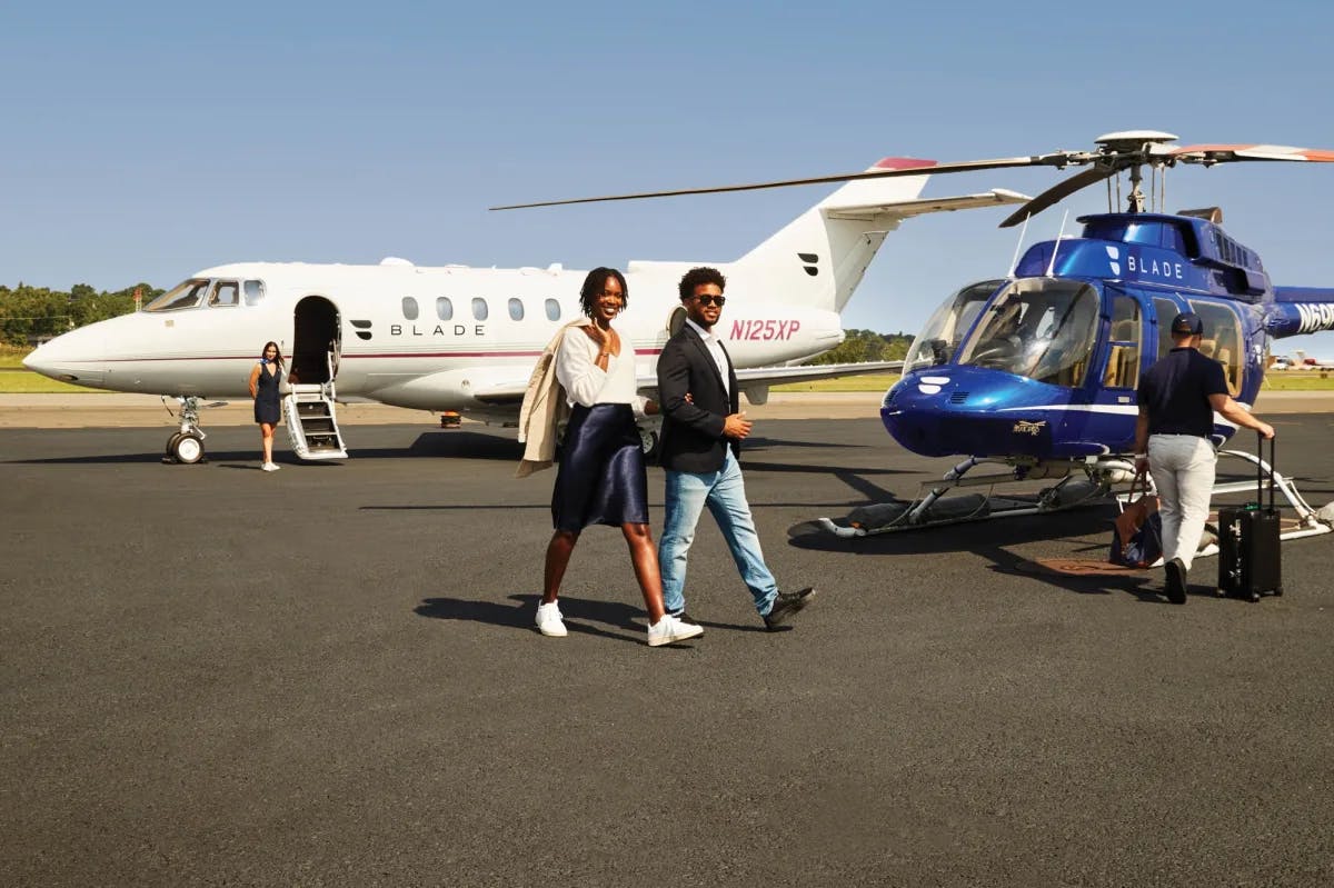 a man and a woman walk from a white jet to a blue helicopter