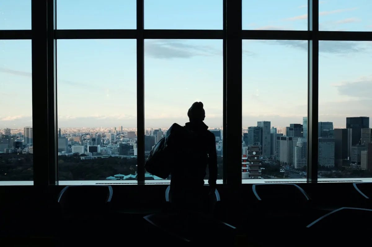Man in airport stares out of a terminal window at an urban skyline