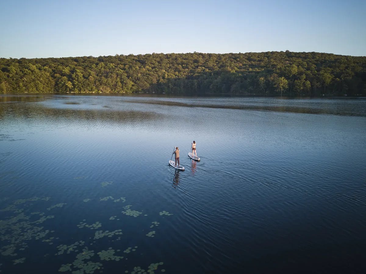 two people stand on paddle boards on a mountain lake