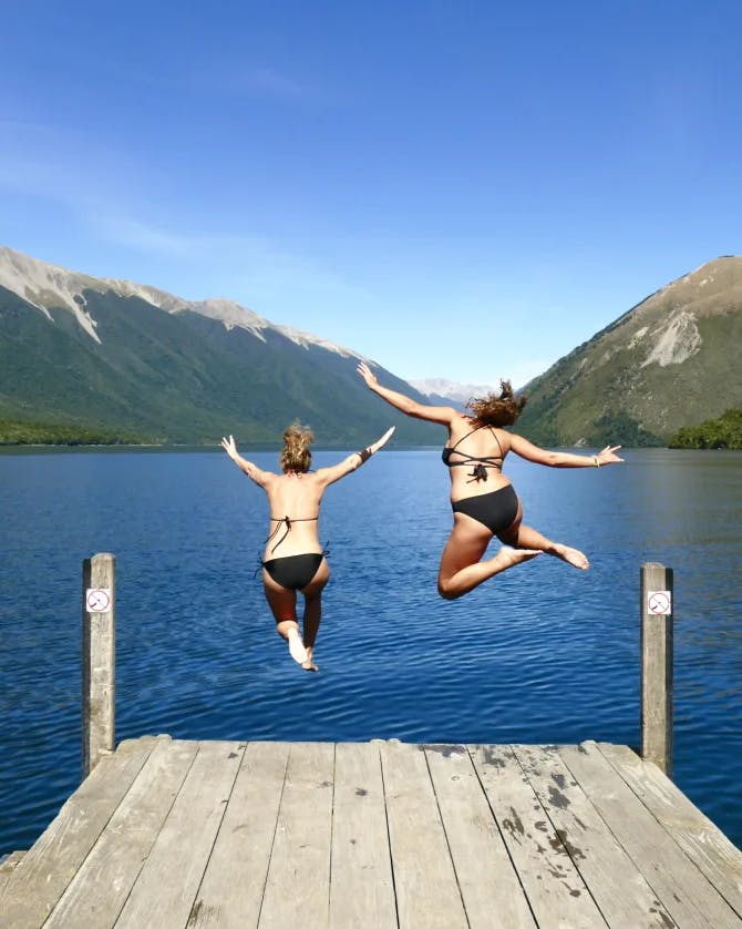 Advisor Jeannie Peters and female companion jumping into the lake from a wooden deck with mountains in view