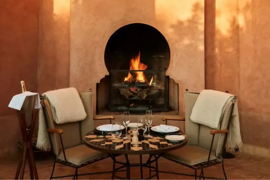 Two Moroccan chairs are set up before an intimate table setting in front of a clay fireplace
