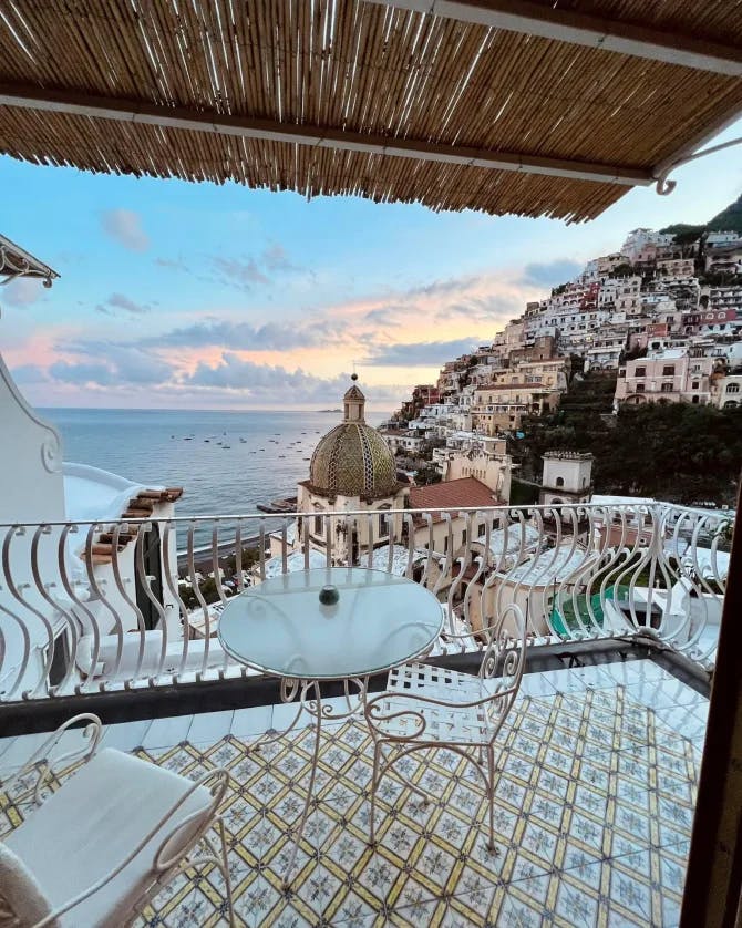 A beautiful view of an outside terrace during sunset with the ocean and a hillside town in the distance. 