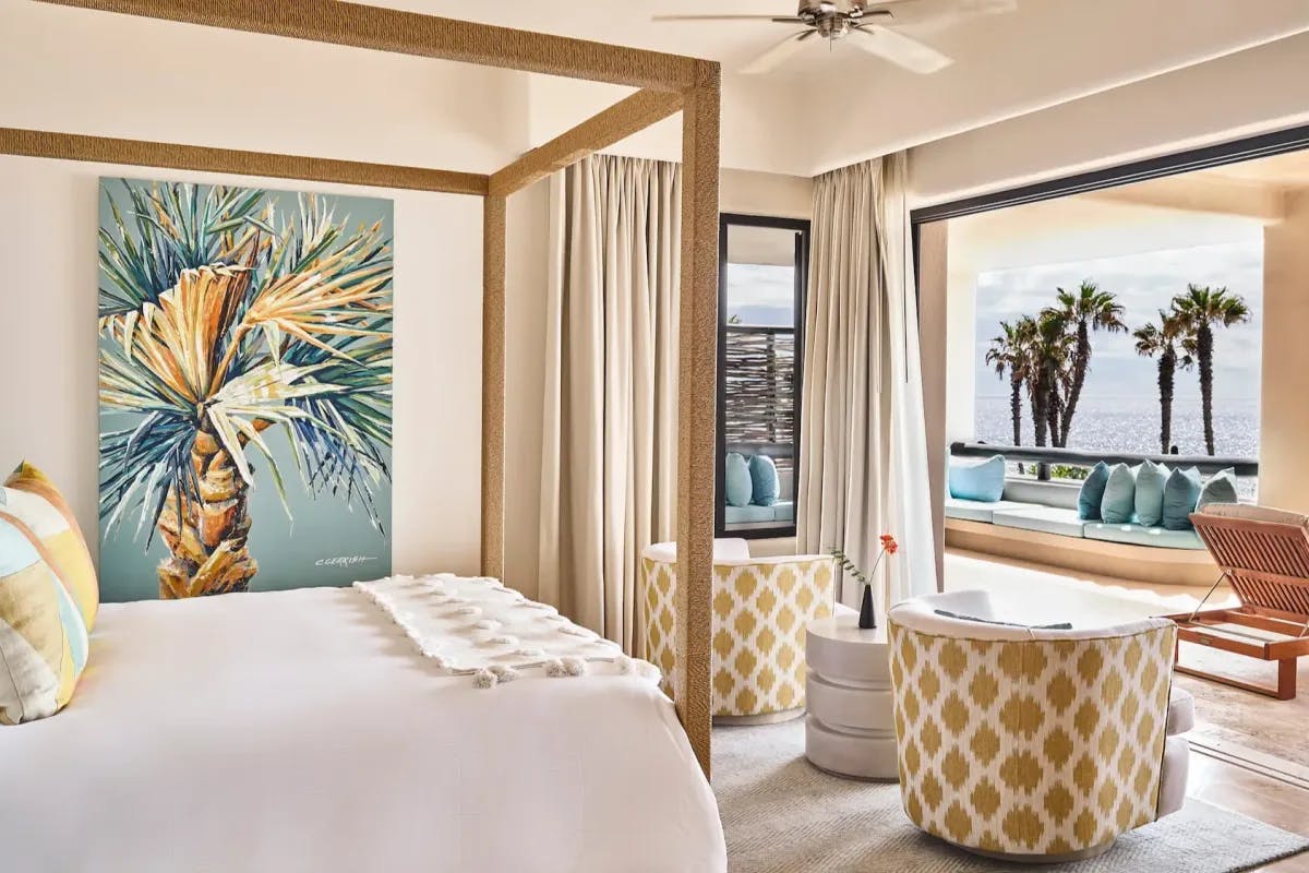 a breezy hotel room with a white four-post bed overlooking the ocean