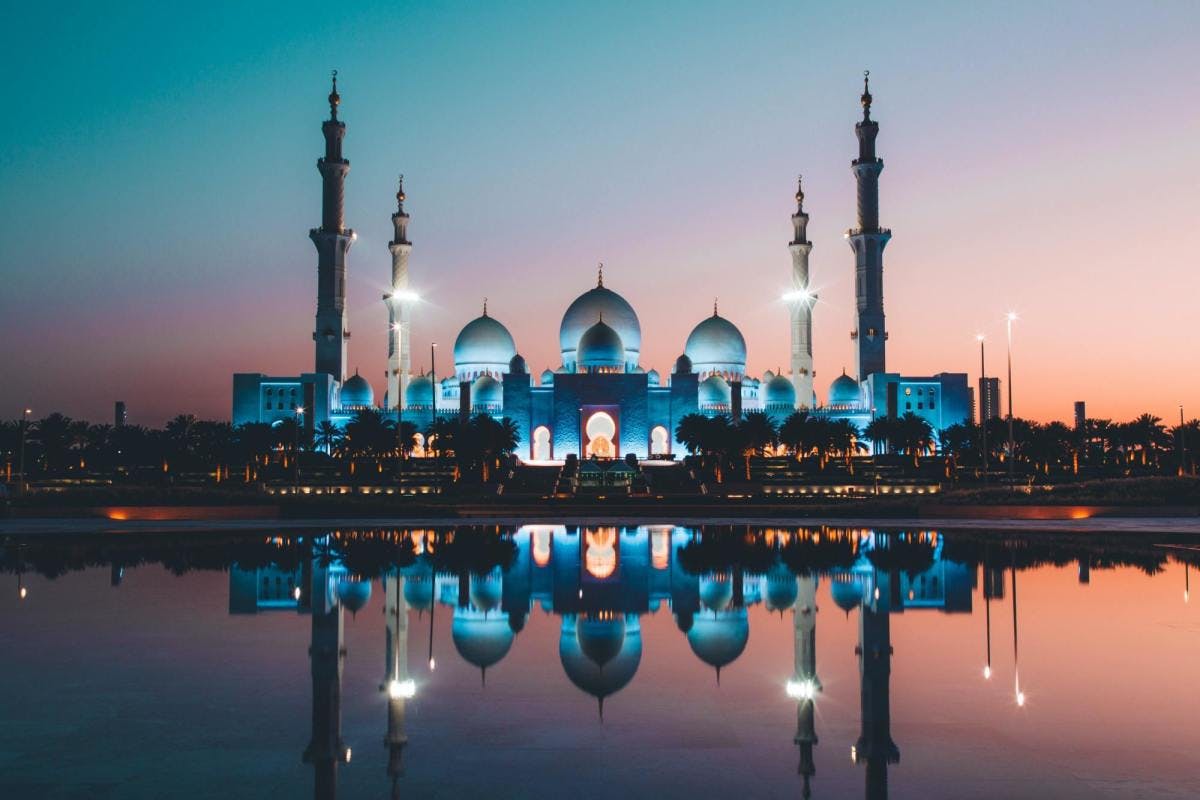 Sheikh Zayed Mosque lit up with blue and white lights with reflection on water during sunset in Abu Dhabi.