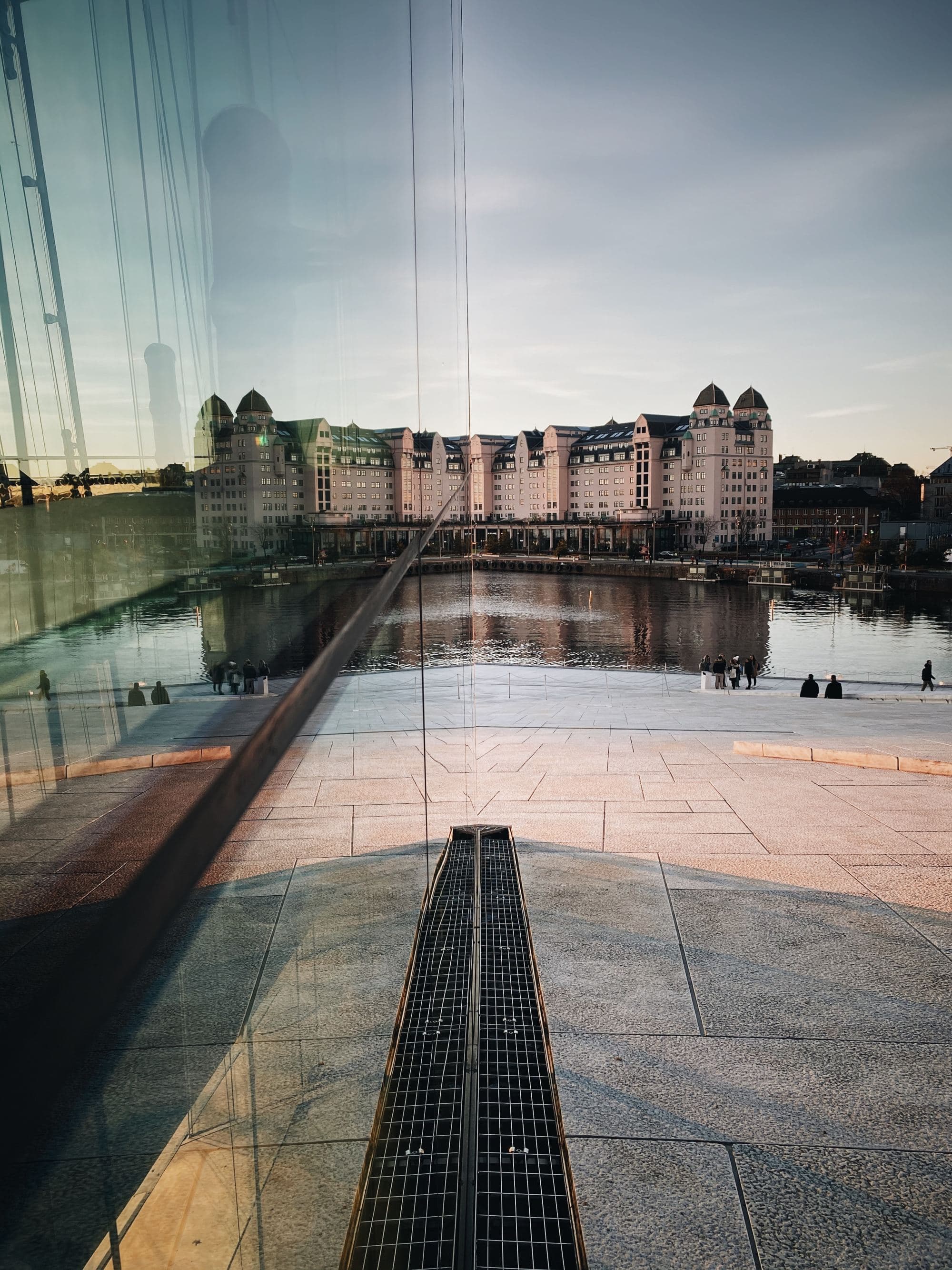 modern glass building on a river with a castle-like building in the distance