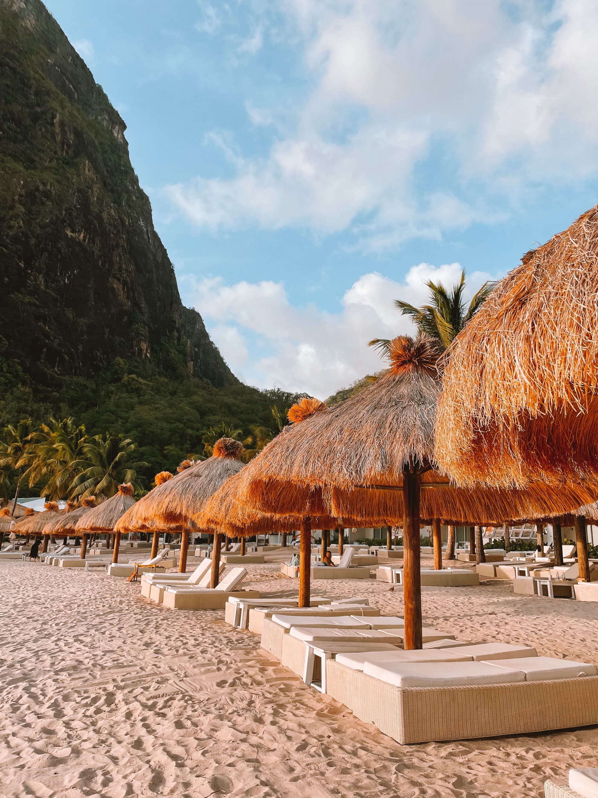 Beach loungers on the sand with straw umbrellas above