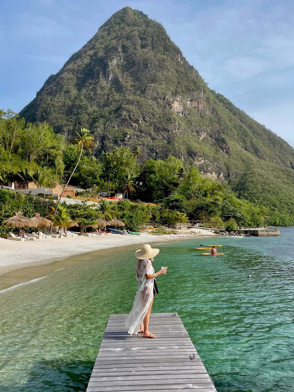 A person standing at the end of a dock in the water with a mountain in the distance