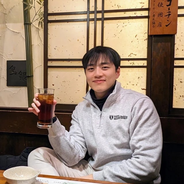 David Xiah posing with a drink in hand inside of a restaurant. 