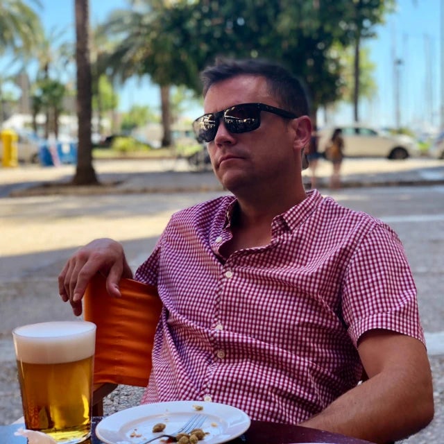 David Bennett in a checkered shirt and sunglasses sitting at an outdoor restaurant enjoying a beer and meal