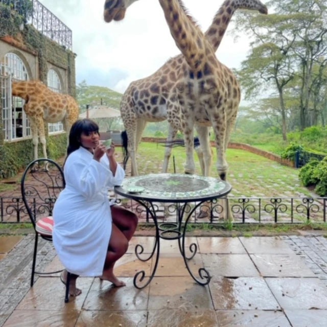 Fora travel agent Valerie Fervil sitting at table with giraffes in the background on a cloudy day