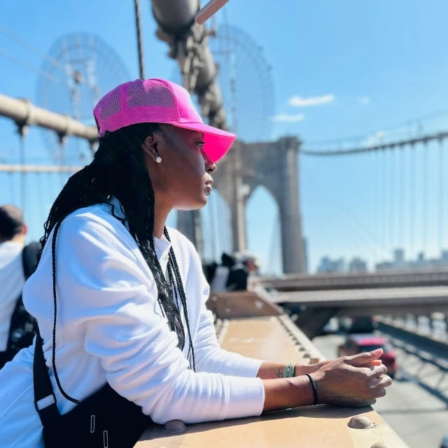 Alexis wearing a white sweater and pink hat on a bridge admiring the view