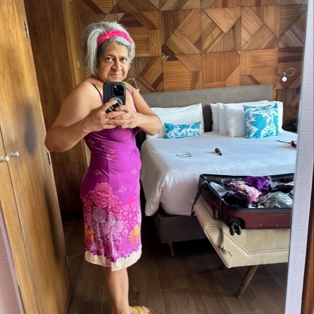 Swati Shah in a pink dress and headband standing in a hotel room with suitcase and be din view