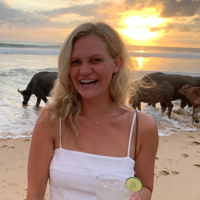 Travel advisor Katie Gooding posing in infront of animals on the beach wearing a white dress.