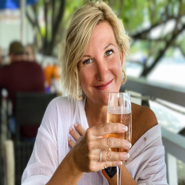 Travel advisor Kristin Rotter wearing a white top and seated outside at a restaurant holding a glass of champagne in her hand. 