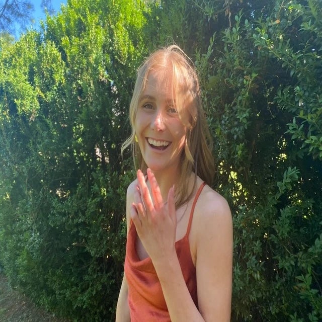 Travel Advisor Emma Wetenhall in orange dress in front of green shrubs.
